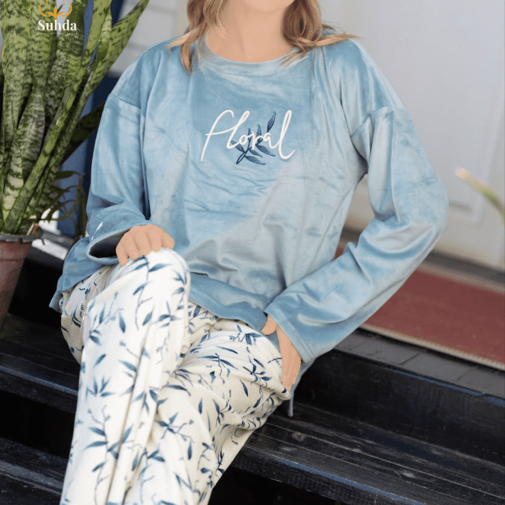 طقم شتوي نسائي بلوزة مخمل سماوية اللون مع بنطال كريمي بنقشة أوراق زرقاء.