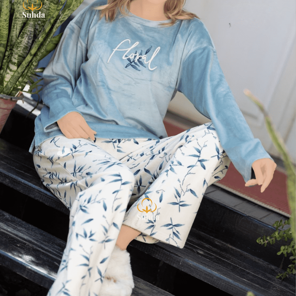 طقم شتوي نسائي بلوزة مخمل سماوية اللون مع بنطال كريمي بنقشة أوراق زرقاء.